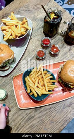 Grand angle de hamburgers avec frites placées sur des assiettes près des bocaux de ketchup et thé froid dans des tasses en verre avec citron et paille dans le café Banque D'Images