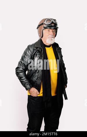 Portrait d'un motard mâle barbu vieilli dans une veste en cuir et un casque de moto, main dans une poche isolée sur fond blanc Banque D'Images