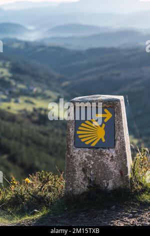 Panneau surmonté d'une météo avec symbole de seashell installé près d'un chemin de pierre étroit contre le ciel nuageux et la crête de montagne sur la route de St James en Galice, Espagne Banque D'Images