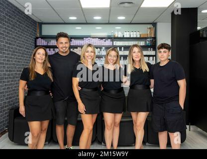 Des hommes et des femmes heureux en uniforme s'embrassant et regardant la caméra avec le sourire pendant le travail dans le salon de coiffure Banque D'Images