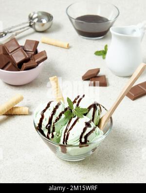 De la crème glacée délicieuse avec un rouleau de gaufres et une feuille de menthe dans un bol en verre servi sur une table près des barres de chocolat et du ganache dans la cuisine Banque D'Images