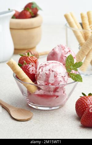De délicieuses glaces aux fraises faites maison servies dans un bol en verre avec petits fruits et gaufres dans la cuisine à la lumière du jour Banque D'Images