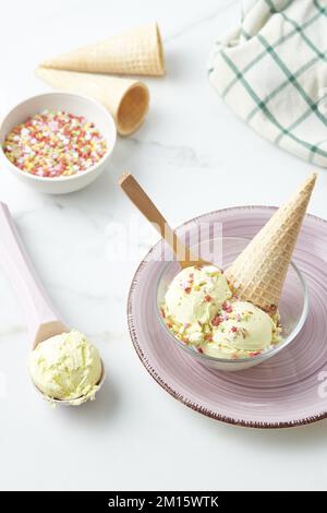Au-dessus d'un bol de délicieux gelato à la vanille maison décoré de saupoudrés en forme d'étoiles colorées et de cornet de gaufres et servi sur table en kit léger Banque D'Images