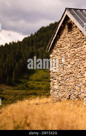 Mur extérieur en pierres avec petite fenêtre et toit sur prairie rurale dans la campagne des Pyrénées montagnes à la lumière du coucher du soleil Banque D'Images