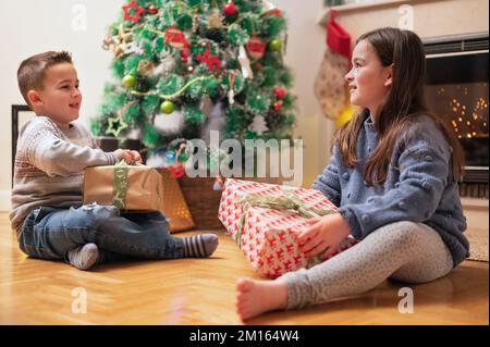 Les enfants heureux ouvrant des cadeaux de noël à la maison près de l'arbre de Noël et de la cheminée. Photographie de haute qualité Banque D'Images