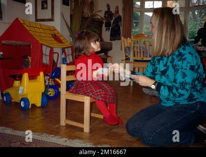 Fille de deux ans assise à la chaise pendant qu'au pair montre ses cartes Flash Surrey Angleterre Banque D'Images