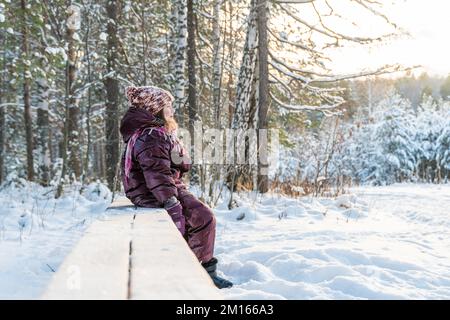 jolie fille sur un banc en hiver dans la forêt enneigée Banque D'Images