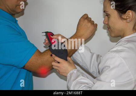 Image d'une physiothérapeute féminine montrant un patient souffrant de douleur à l'épicondylite comment mettre sur le corset. soulagement de douleur de coude de tennis Banque D'Images