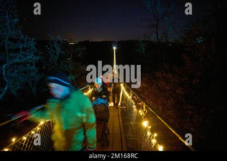 10 décembre 2022, Rhénanie-Palatinat, Mörsdorf : les visiteurs traversent le pont de corde lumineux de 360 mètres de long Geierlay après la tombée de la nuit. Plus de 7000 lampes LED éclairent l'aimant touristique à Hunsrück pendant l'événement "GeierLights". Photo: Thomas Frey/dpa Banque D'Images