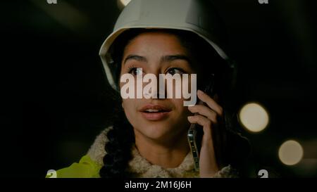 Jeune femme arabe professionnelle ingénieur technique architecte constructeur en uniforme et hardhat parlant téléphone mobile avec le travailleur de bâtiment discutant Banque D'Images