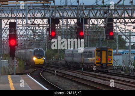 Avanti West Coast Pendolino train et transport pour le sprinter du pays de Galles en passant à la jonction sud de Crewe avec des signaux rouges sur un portique Banque D'Images