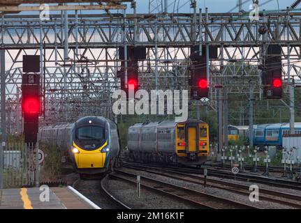 Avanti West Coast Pendolino train et transport pour le sprinter du pays de Galles en passant à la jonction sud de Crewe avec des signaux rouges sur un portique Banque D'Images