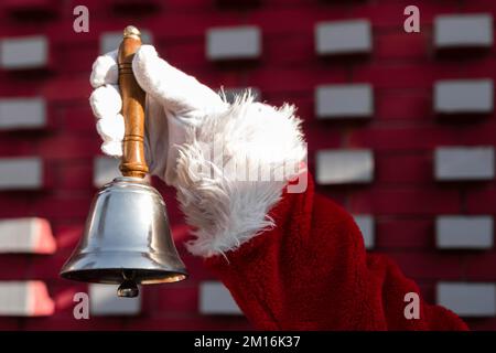 Gros plan d'une main de Père Noël tenant une cloche de Noël Banque D'Images