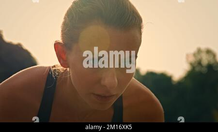 Jeune femme motivée coureur caucasien jogger femelle assis en position courbée sur la ligne de départ prêt à courir course marathon préparation pour sprint course prac Banque D'Images