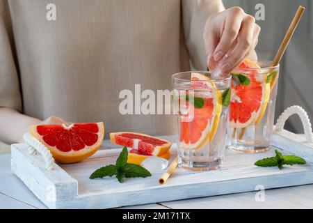 Une jeune fille prépare un cocktail de fruits frais d'été avec des tranches de pamplemousse et de la menthe. Banque D'Images