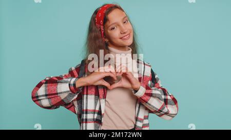 Je t'aime. Sourire jeune adolescent fille enfant fait coeur geste démontre signe d'amour exprime de bons sentiments et de la sympathie. Enfants de 12 ans préadolescents isolés sur fond de mur bleu de studio Banque D'Images