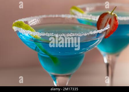 Deux verres avec cocktail de margarita bleue garni de zeste de lime et de fraises, foyer sélectif. Banque D'Images