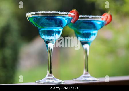 Deux verres avec cocktail de margarita bleue garni de zeste de lime et de fraises, foyer sélectif. Banque D'Images