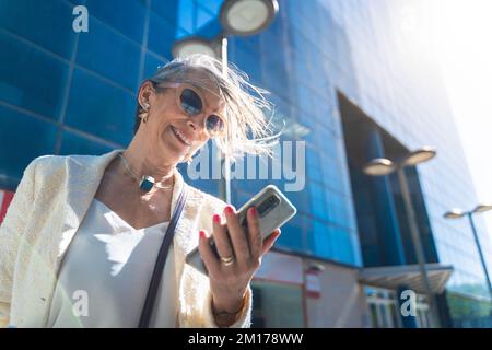 Femme d'affaires d'âge moyen attrayante regardant son smartphone dans la rue. Banque D'Images
