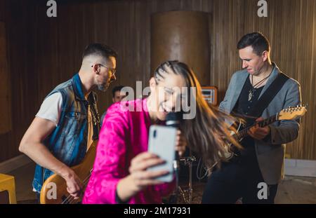 groupe de musique se présentant à répétition et une chanteuse-fille enregistrant une vidéo en direct, studio de musique deux guitaristes, un chanteur et un batteur. Photo de haute qualité Banque D'Images