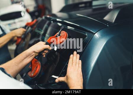 Les ventouses de glace sont nécessaires dans le kit de réparation de pare-brise et de lunette arrière. Mains de deux mécaniciens caucasiens non reconnaissables qui retirent la lunette arrière de la voiture noire. Photo de haute qualité Banque D'Images