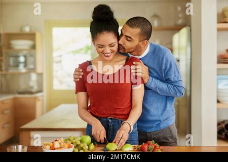 Se soutenir mutuellement pour être le plus sain possible. Photo d'un jeune homme embrassant sa femme pendant qu'elle prépare un en-cas sain à la maison. Banque D'Images