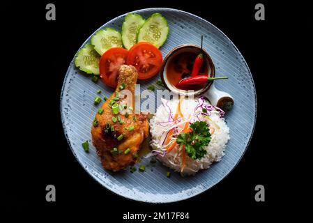 Cuisse de poulet rôtie de style vietnamien avec riz, légumes et sauce isolée sur fond noir vue du dessus Banque D'Images