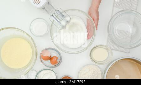 Les blancs d'œufs fouettés sont rapprochés dans un bol en verre. Recette de gâteau au chocolat étape par étape, processus de cuisson. Arrière-plan de table de cuisine blanc, femme avec copie Banque D'Images