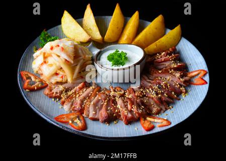 Filet d'oie frit à l'ail servi avec des quartiers de pommes de terre et du kim chi sur fond noir vue du dessus Banque D'Images