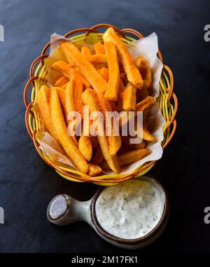 Frites au cheddar dans un panier avec sauce à l'ail crémeuse sur fond noir vue du dessus Banque D'Images