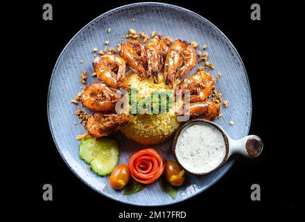 Crevettes grillées au riz et aux légumes frits sur une assiette bleue isolée sur fond noir vue du dessus Banque D'Images