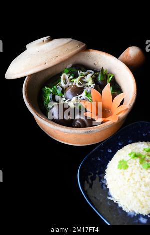 Escargots bouillis farcis de porc dans un pot avec des légumes sur fond noir sidevers Banque D'Images