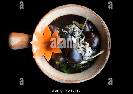 Escargots bouillis farcis de porc dans un pot avec des légumes sur fond noir sidevers Banque D'Images