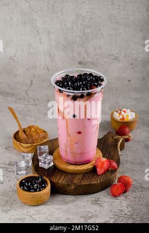 Boba ou perles de tapioca est le thé de lait à bulles de taïwan dans une tasse en plastique avec saveur de confiture de fraise sur fond de texture, rafraîchissement d'été. Banque D'Images