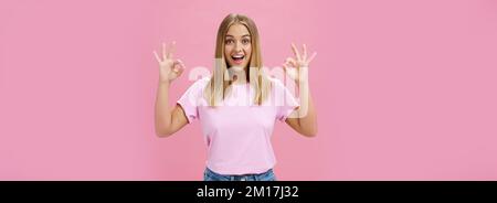 Portrait de la jeune fille caucasienne attrayante et enthousiaste en t-shirt à la mode et jeans montrant bon ou confirmer le geste avec un large sourire amusé debout Banque D'Images
