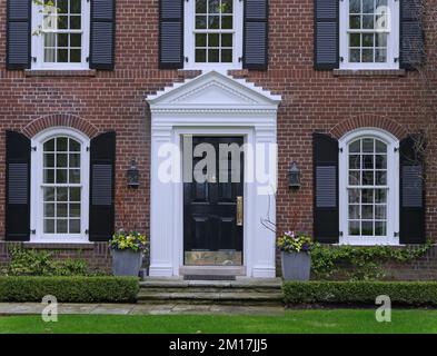 Porte d'entrée de la maison traditionnelle en brique de deux étages avec des volets noirs à côté des fenêtres Banque D'Images