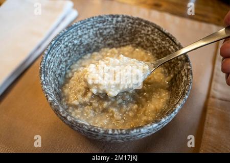 Flocons d'avoine entiers, grand bol de porridge avec beurre pour le petit-déjeuner, repas du matin. Vue de dessus, gros plan, table grise. Végétalien régime sain et savoureux. Banque D'Images