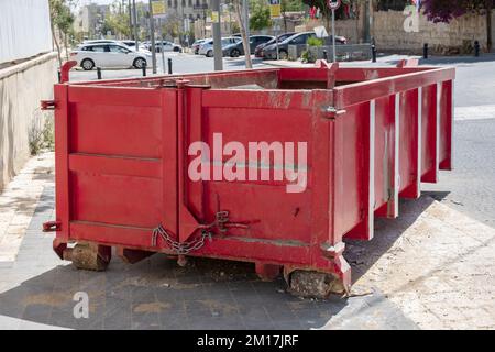 Déchets de construction dans une benne à moitié vide Red. Conteneur de déchets métalliques rempli de déchets de construction, en caoutchouc près d'un chantier de construction. Banque D'Images