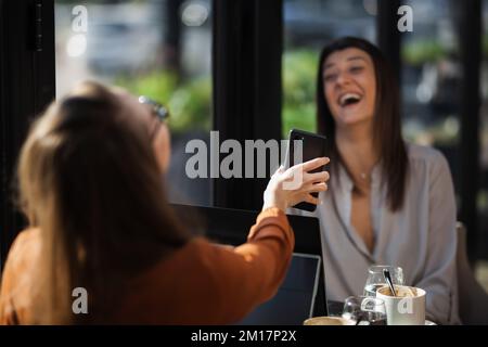 Deux jeunes femmes d'affaires dans un café ayant un sur une réunion. Amis après le travail parlant de gossiping et d'avoir le café à une table de fenêtre avec réflexion Banque D'Images