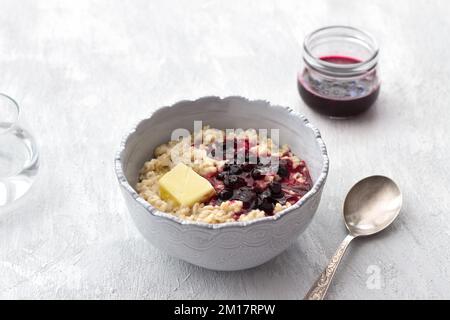 Délicieux porridge de flocons d'avoine avec beurre et confiture dans un bol gris sur fond gris clair. petit déjeuner maison sain. mise au point sélective, espace Banque D'Images