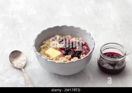Délicieux porridge de flocons d'avoine avec beurre et confiture dans un bol gris sur fond gris clair. petit déjeuner maison sain. mise au point sélective, espace Banque D'Images