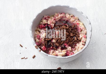 Délicieux porridge de flocons d'avoine avec beurre, confiture et chocolat râpé dans un bol gris sur fond gris clair. petit déjeuner maison sain. mise au point sélective, s Banque D'Images