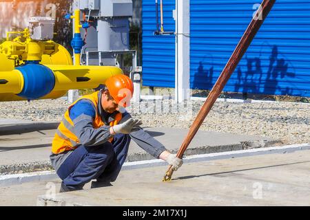 Le Slinger pose une dalle de béton sur le chantier de construction le jour de l'été. Le travailleur dans la veste de protection et le casque de construction supervise la pose de la base sur le chantier. Banque D'Images
