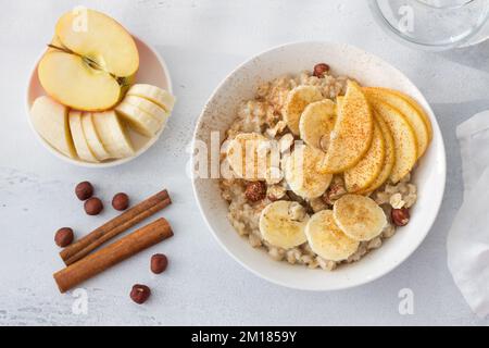 Délicieux petit déjeuner sain. Flocons d'avoine avec banane, pomme, noix et cannelle sur fond gris clair, vue du dessus Banque D'Images