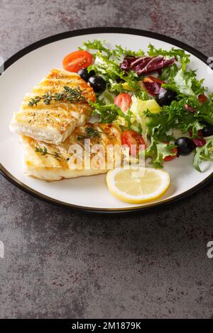 Morue grillée avec salade de tomates fraîches, olives, salade mélanger en gros plan dans une assiette sur la table. Verticale Banque D'Images