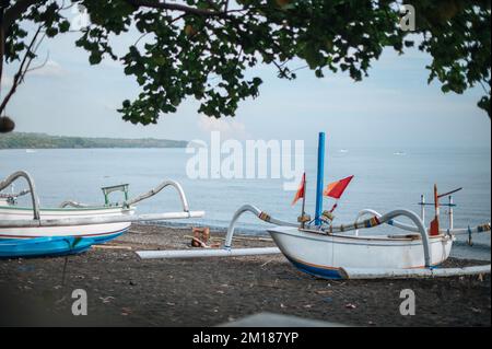 Vue aérienne de la plage d'Amed à Bali, Indonésie. Des bateaux de pêche traditionnels appelés jukung sur la plage de sable noir et le volcan du mont Agung Banque D'Images