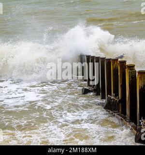 Vagues se brisant sur une groyne avec un mouette assis sur un poteau Banque D'Images