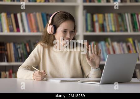 Bonne fille étudiante dans le casque appréciant étudier dans la bibliothèque Banque D'Images