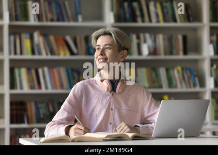 Joyeux adolescent asiatique étudiant faire ses devoirs dans la bibliothèque de l'université Banque D'Images