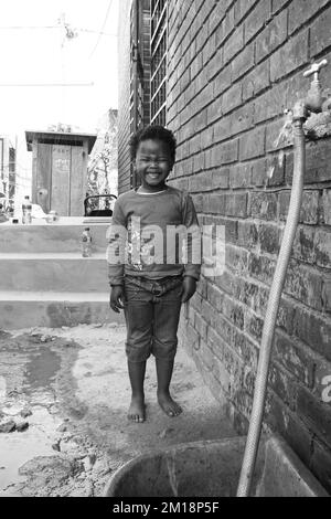 Une photo en niveaux de gris d'une petite fille africaine éclaboussé par l'eau d'un demi-tube Banque D'Images